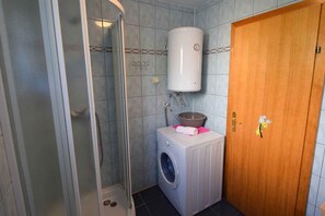Une salle de bain avec une douche, un lave-linge et des toilettes.