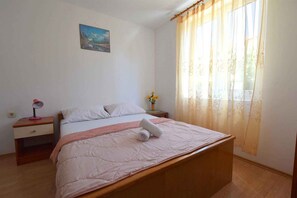 Une chambre Ă coucher avec un lit, une table de chevet, une lampe, un vase de fleurs et un tableau au mur.
