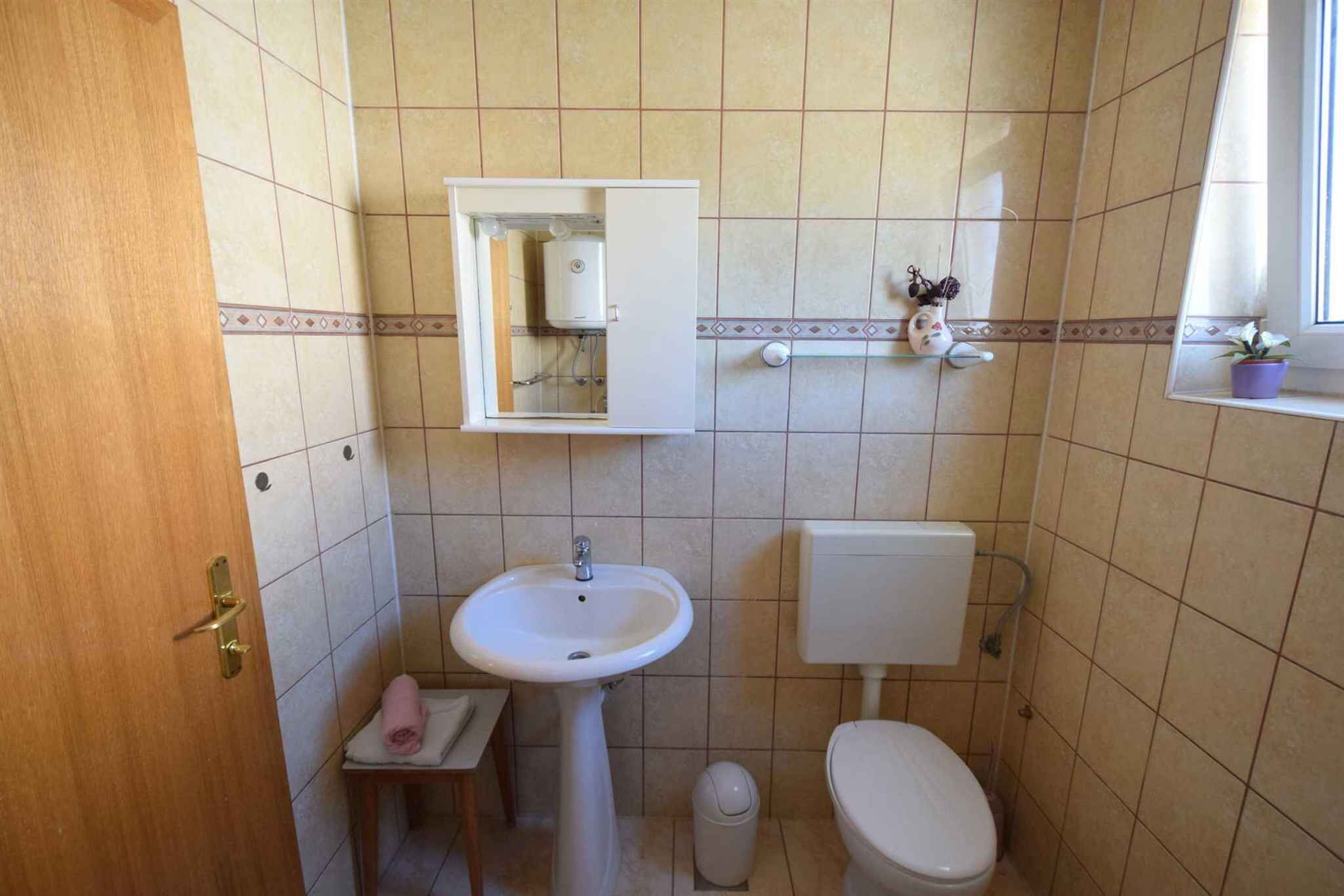 Een badkamer met een wit wastafel, toilet en een klein raam met een plant.