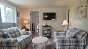 A living room with two plaid sofas, a white coffee table, and a TV mounted on the wall. - Quaint Farmhouse on  Palisade Peach Orchard close to Wineries (Palisade)