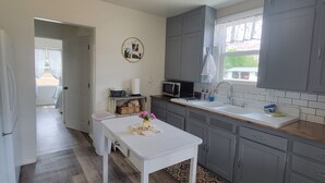 A kitchen with grey cabinets, a white countertop, and a wooden floor. There is a table with a vase of flowers and a picture frame on the wall. - Quaint Farmhouse on  Palisade Peach Orchard close to Wineries (Palisade)
