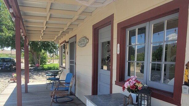 A covered porch with a table and chairs, a welcome sign, and a window with a view. - Quaint Farmhouse on  Palisade Peach Orchard close to Wineries (Palisade)