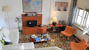 A living room with a white sofa, orange chairs, a TV, a map, and a lamp.