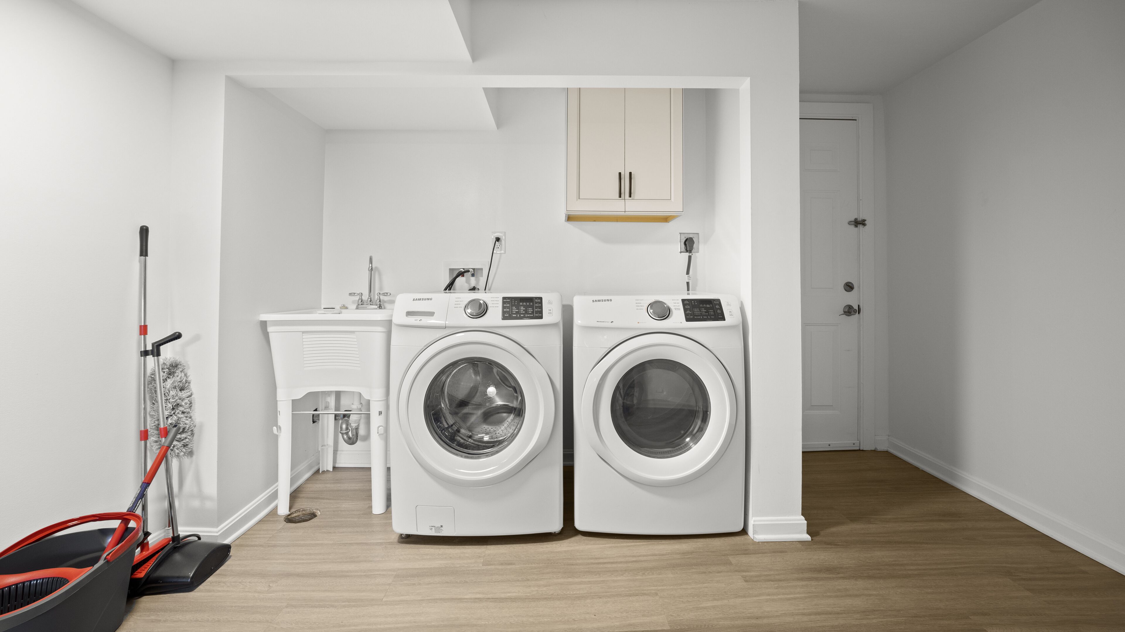 A laundry room with two white washing machines, a sink, and a mop.