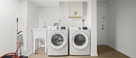 A laundry room with two white washing machines, a sink, and a mop.