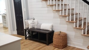 Un escalier avec des rampes blanches et des marches en bois, un banc sombre agrémenté de coussins et un panier tressé posé sur un plancher en bois.