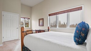 Ein Schlafzimmer mit einem großen Bett, einem Fenster mit Jalousien, einer Tür und einem gerahmten Bild an der Wand.