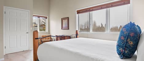 Een slaapkamer met een groot bed, een raam met zonwering, een deur en een ingelijst kunstwerk aan de muur.