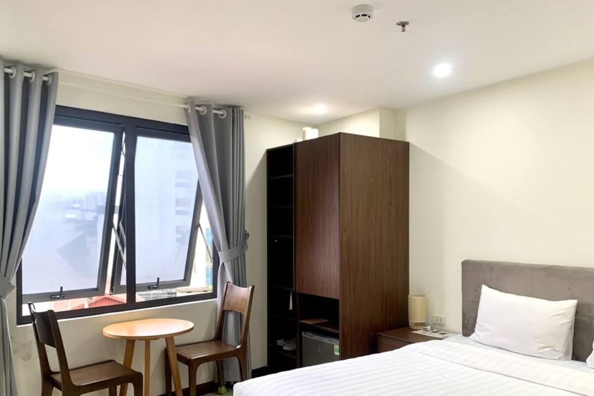 Habitación de hotel con cama, escritorio con silla, armario y ventana con cortinas.