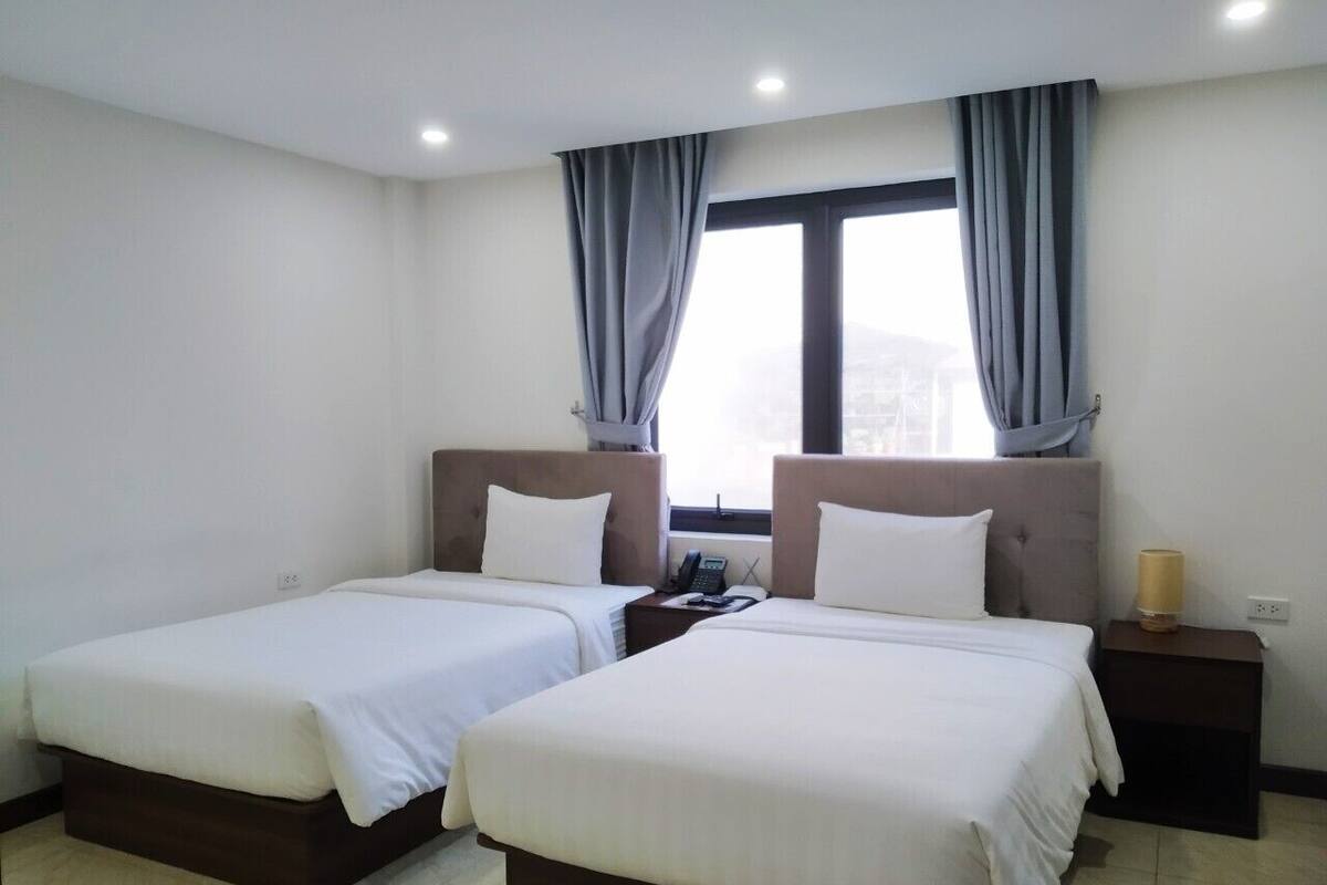 Habitación de hotel con dos camas individuales, una mesita de noche con lámpara, teléfono y ventana con cortinas.