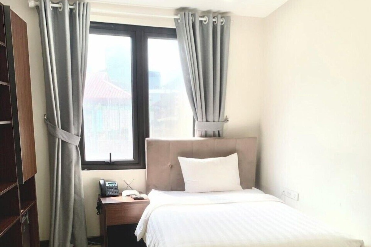 Een hotelkamer met een bed, nachtkastje, gordijnen en een raam met uitzicht.