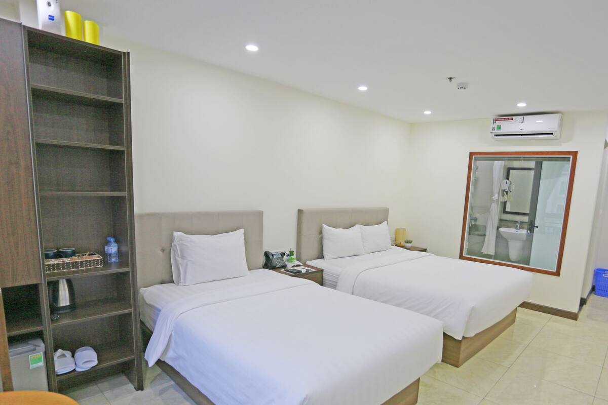 Habitación de hotel con dos camas, un armario, baño con espejo y aire acondicionado.