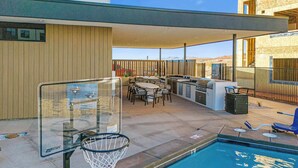 An outdoor pool area with a basketball hoop, a barbecue grill, and a seating area with tables and chairs. - Spacious 2-Bed Suite | Sunset Views, Private Patio & Fireplace (Hurricane)