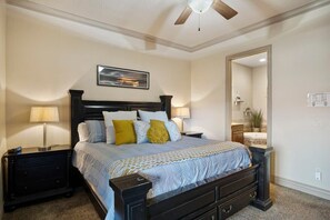 A bedroom with a bed, nightstands, a ceiling fan, a mirror, and a wall-mounted light fixture. - Spacious 2-Bed Suite | Sunset Views, Private Patio & Fireplace (Hurricane)