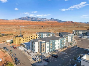 A multi-story building with a parking lot, surrounded by a desert landscape with mountains in the background.