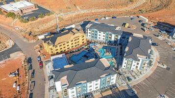 An aerial view of a hotel complex with multiple buildings, parking areas, and a swimming pool.
