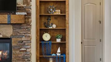 A room with a stone fireplace, wooden shelves with nautical decorations, and a closed door.