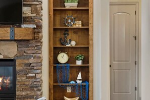 A room with a stone fireplace, wooden shelves with nautical decorations, and a closed door. - Spacious 2-Bed Suite | Sunset Views, Private Patio & Fireplace (Hurricane)