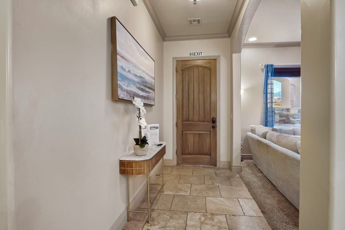 A hallway with a wooden door marked 'EXIT', a console table with a vase, and a couch in the background.