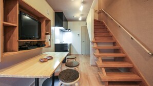 A modern interior with a wooden staircase, a dining area with a table and stools, and a kitchen in the background. - Yadoya Iriyaan (Tokyo)