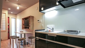 A compact kitchen with a black countertop, a built-in oven, and a small dining area with stools. - Yadoya Iriyaan (Tokyo)