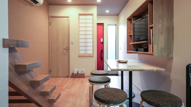 A compact kitchen with a wooden staircase, a dining area with stools, and a TV mounted on the wall. - Yadoya Iriyaan (Tokyo)