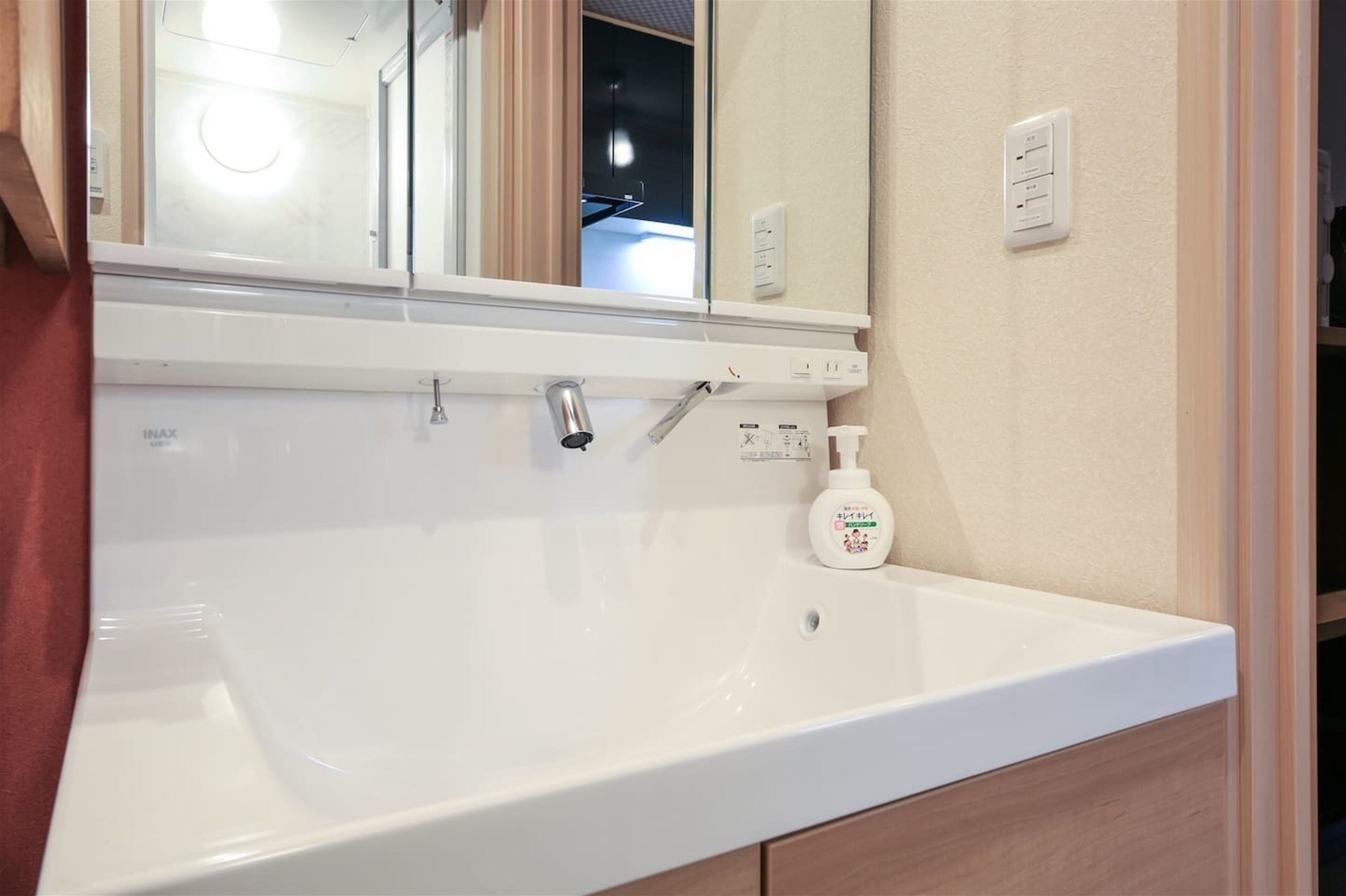 A bathroom with a white sink, a mirror, and a bottle of hand soap.