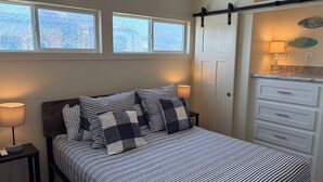 Un dormitorio con cama, mesitas de noche, cómoda y ventana con vidrio esmerilado.