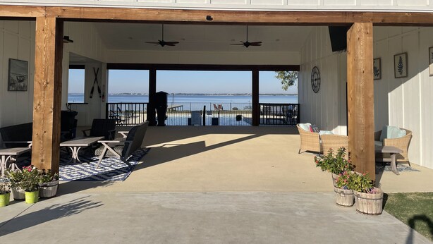 Un patio cubierto con mobiliario exterior, vistas al mar y un edificio con fachada blanca y vigas de madera.