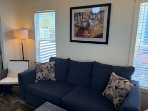 A living room with a dark blue sofa, two patterned throw pillows, a floor lamp, and a framed artwork on the wall. - Lakefront Tiny Home with Dock & View (Kerens)