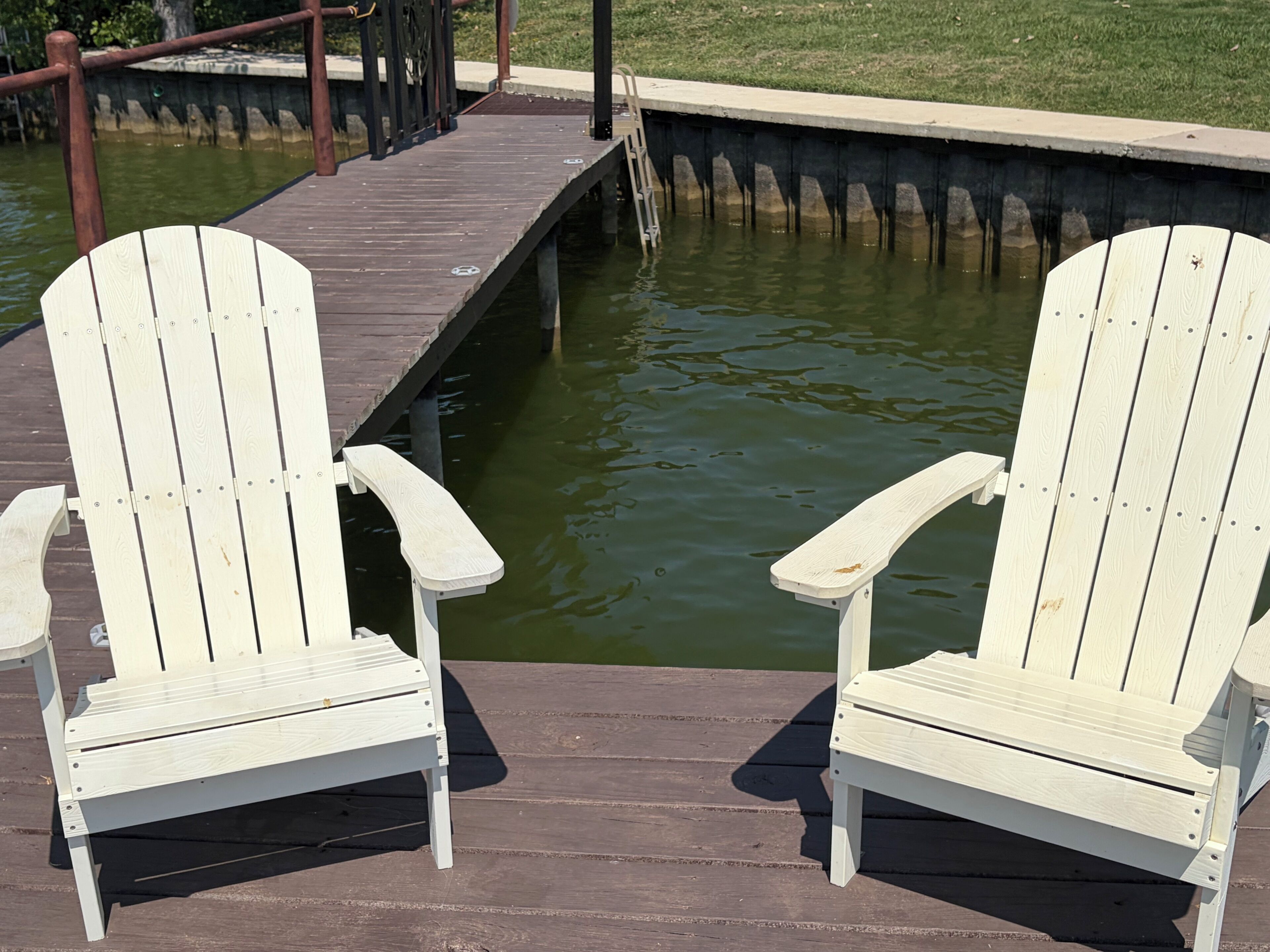 Deux chaises Adirondack blanches sont posées sur une jetée en bois qui s’avance sur une étendue d’eau.