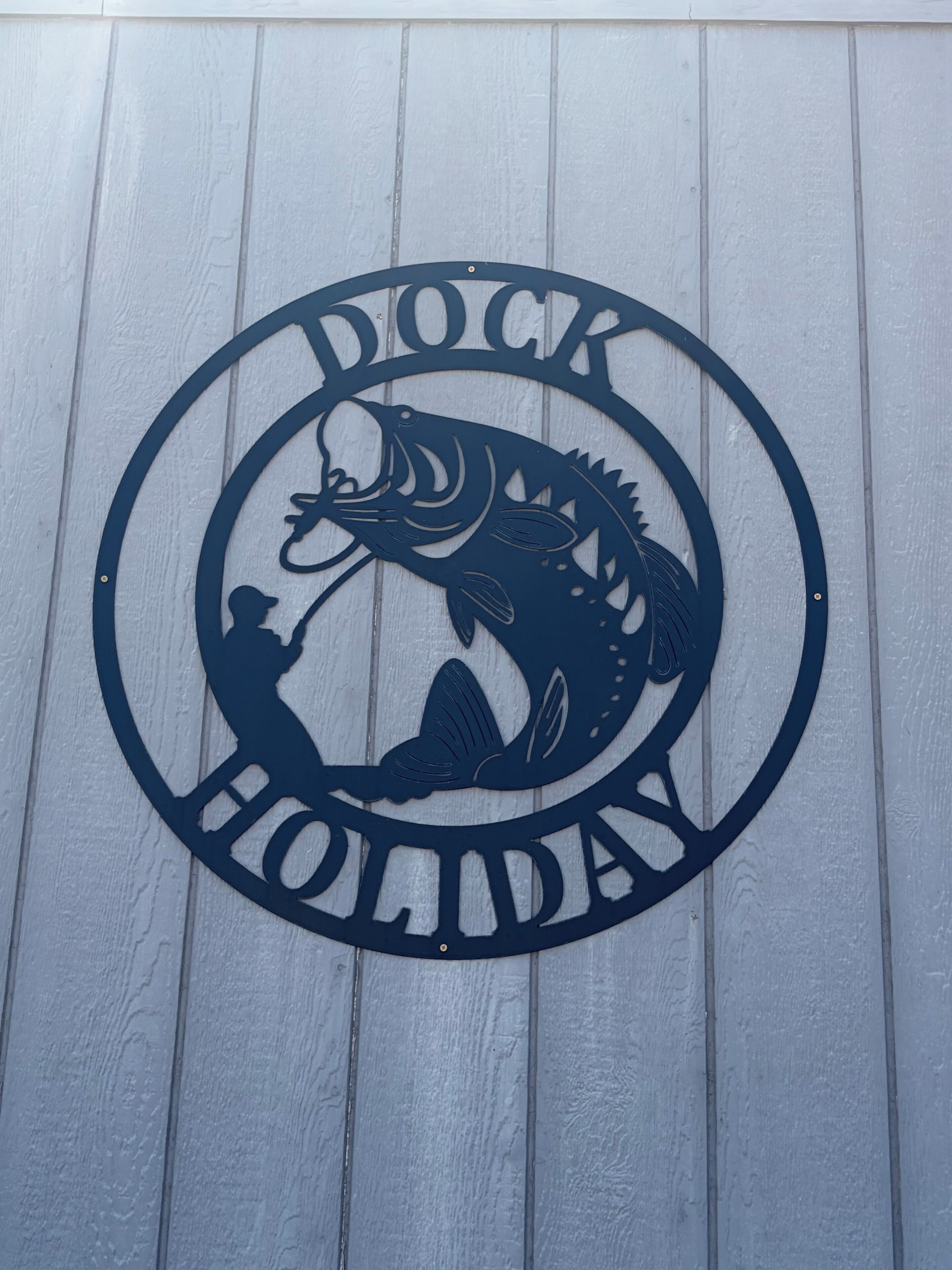 A circular metal sign with a fish and a person fishing, and the words 'Dock Holiday' around it.