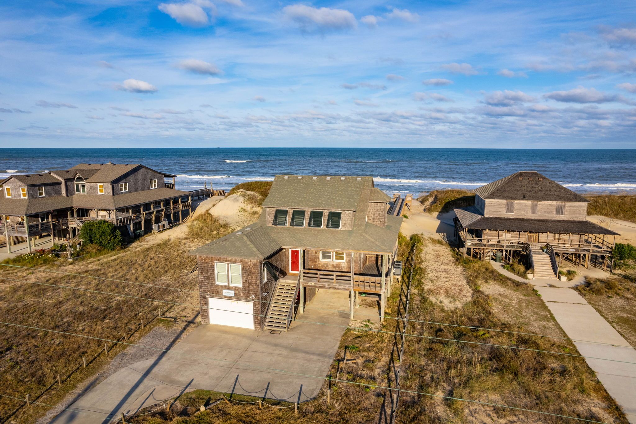 A coastal property with multiple buildings, including a main house with a garage, a smaller structure with a red door, and a wooden building with a thatched roof.