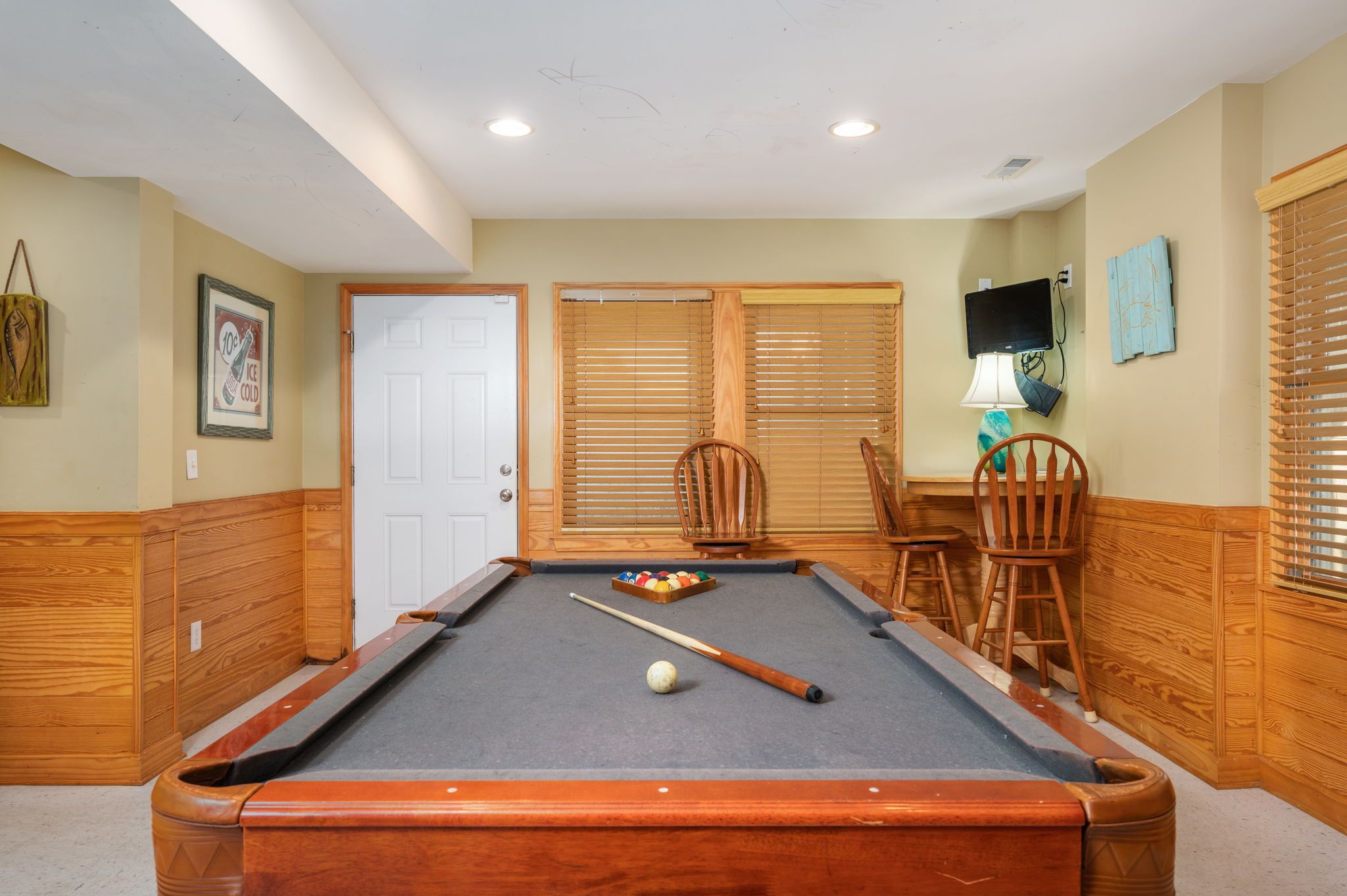 A pool table with a cue stick, a ball, and a set of billiard balls. There are wooden chairs and a wooden bench.