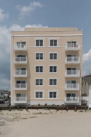 A multi-story building with balconies, a flat facade, and a sandy ground in front.
