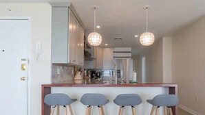 Une cuisine moderne avec un îlot central, des tabourets de bar, des luminaires suspendus et une porte blanche.
