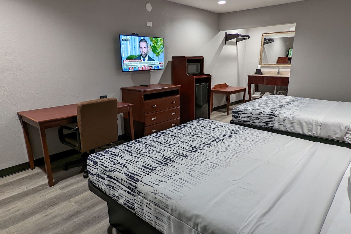 A hotel room with two beds, a desk, a dresser, a television, and a mirror.