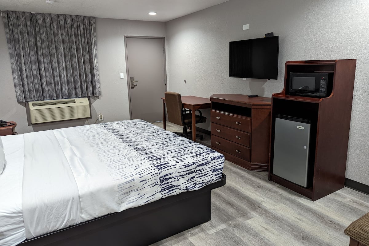 A hotel room with a bed, a desk, a television, a microwave, and a refrigerator.