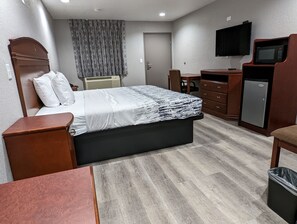 A hotel room with a bed, a desk, a chair, a TV, and a mini-fridge. - OKC Hotel (Oklahoma City)