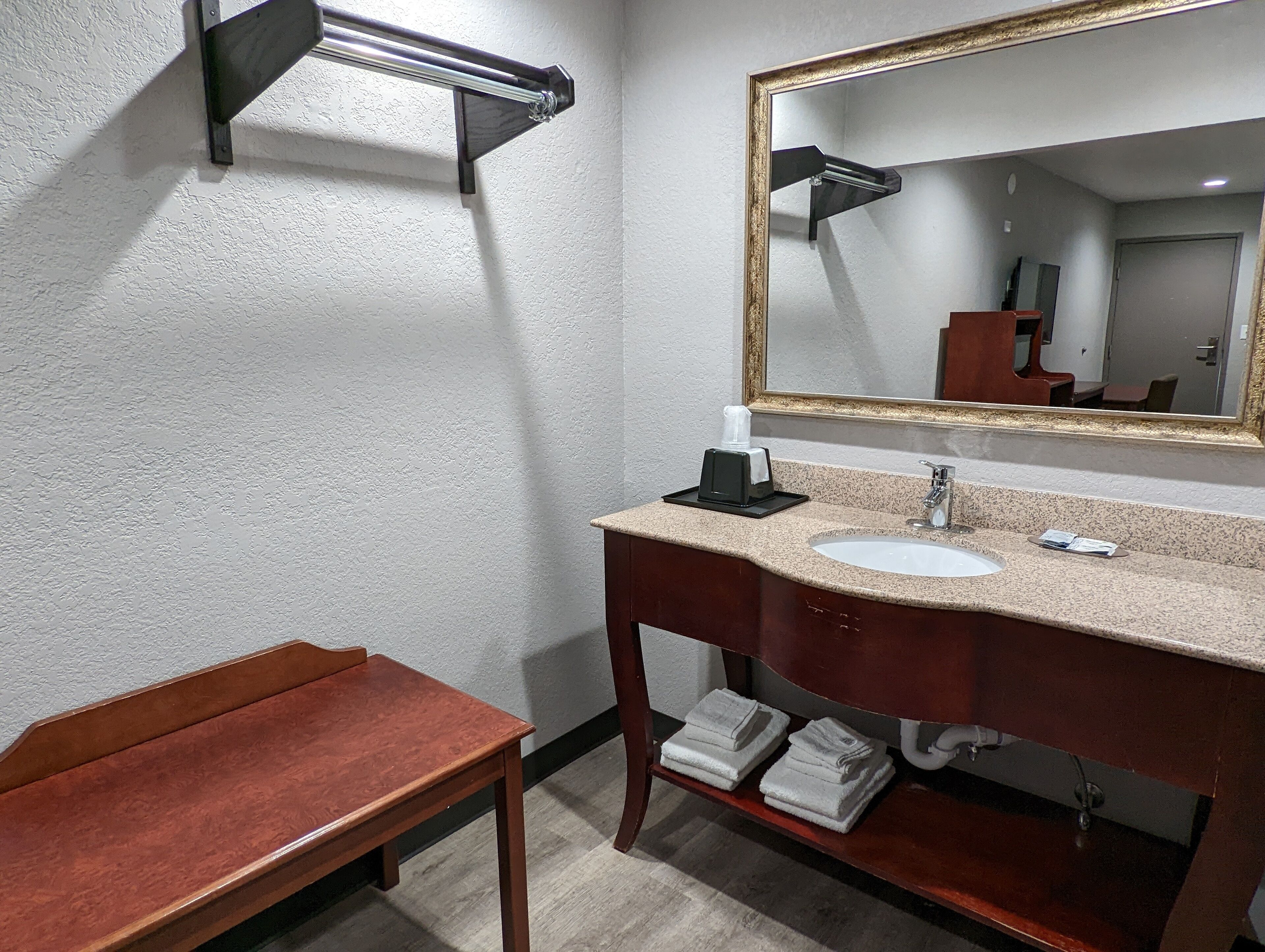 A bathroom with a wooden bench, a sink with a mirror, and towels on the floor.