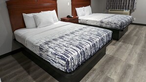 A hotel room with two beds, each with a wooden headboard, white bedding, and a patterned bedspread. There is a nightstand with a phone and a wall-mounted heater. - OKC Hotel (Oklahoma City)
