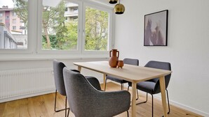 Un espace repas moderne avec une table en bois et des chaises à revêtement gris, un vase et un tableau encadré au mur.
