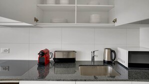 Une cuisine moderne avec des meubles blancs, un grille-pain en acier inoxydable, une bouilloire et un évier.