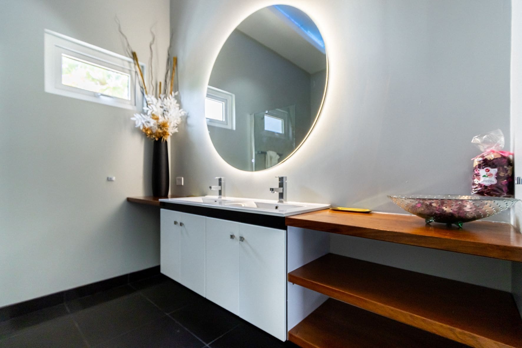 A modern bathroom with a round mirror, white cabinetry, and a wooden countertop.