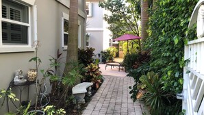 A narrow brick pathway flanked by lush greenery and a white fence.