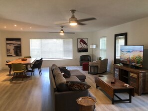 Ein modernes Wohnzimmer mit Essbereich, einer Couch, einem Fernseher und einem Deckenventilator.
