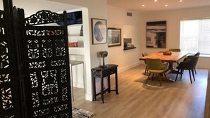A modern dining area with a wooden table and chairs, a decorative black screen door, and framed artwork on the walls.