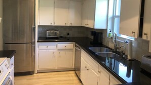 A modern kitchen with stainless steel appliances, white cabinetry, and a black countertop.