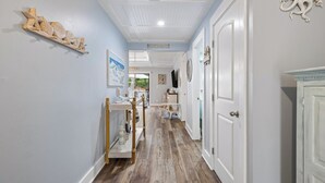 Un couloir avec un plancher en bois, une étagère ornée d’objets décoratifs et une pancarte indiquant « Bienvenue à la plage ».
