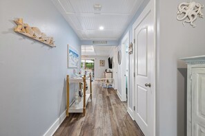 A hallway with a wooden floor, a shelf with decorative items, and a 'Welcome to the Beach' sign.